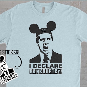 Puede incluir: Una camiseta azul claro con una imagen en blanco y negro de un hombre con orejas de Mickey Mouse. El texto "I DECLARE BANKRUPTCY!" está impreso debajo de la imagen. Se incluye una pegatina gratuita con la camiseta.