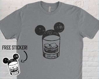 Könnte beinhalten: Graues T-Shirt mit einem schwarzen Aufdruck eines Whiskeyglases mit Eiswürfeln, gekrönt von Mickey Mouse Ohren. Das Wort "Whiskey" ist auf dem Glas aufgedruckt. Ein Aufkleber mit dem gleichen Design ist enthalten.