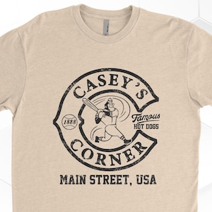 May include: A tan t-shirt with a black and white vintage logo that says "Casey's Corner" with a baseball player holding a bat and a baseball. The logo also says "Famous Hot Dogs" and "Main Street, USA".