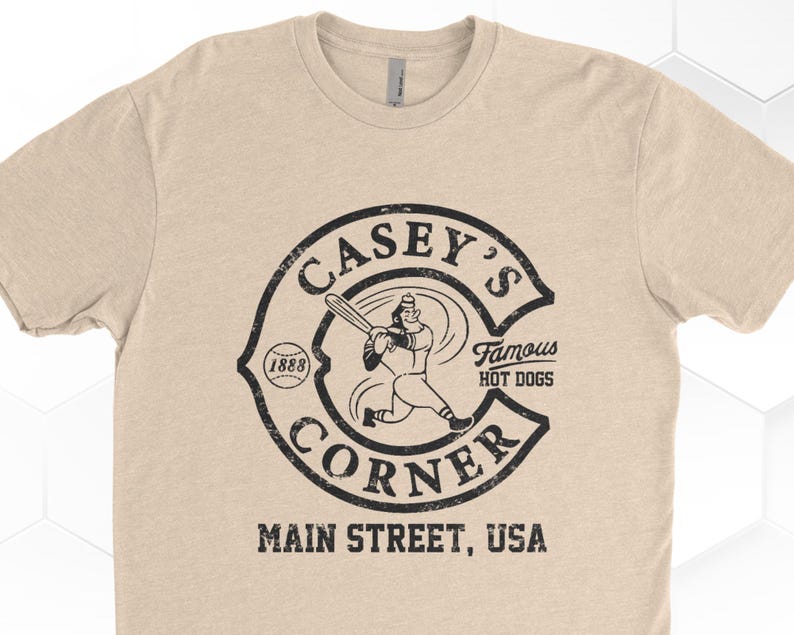 K&ouml;nnte beinhalten: Ein beiges T-Shirt mit einem schwarz-wei&szlig;en Vintage-Logo, auf dem "Casey's Corner" steht, mit einem Baseballspieler, der einen Schl&auml;ger und einen Baseball h&auml;lt. Das Logo sagt auch "Famous Hot Dogs" und "Main Street, USA".