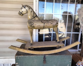 May include: A vintage wooden rocking horse with a light brown and white paint finish. The horse has a saddle and stirrups and is on a wooden base with wheels.