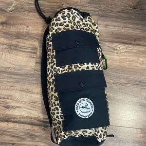 Könnte beinhalten: Eine schwarze Tasche mit Leopardenmuster und Kordelzug mit einer großen schwarzen Tasche auf der Vorderseite. Die Tasche hat eine kleinere schwarze Tasche oben und einen weißen runden Aufnäher mit dem Text "Head Case Helmets & Chopper Supply" und einem Blitz und einem Helm-Motiv.