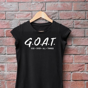 May include: Black t-shirt with white text that reads "G.O.A.T. GOD OVER ALL THINGS"