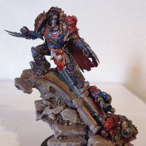 May include: A detailed miniature figure of a warrior in blue and red armor, posed on a rocky terrain. The figure is holding a blade and is surrounded by other fallen figures. The base is a dark circle.