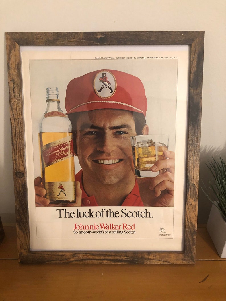May include: A vintage advertisement for Johnnie Walker Red Label Scotch whisky. The ad features a man wearing a red cap with the Johnnie Walker logo and holding a glass of scotch. The text reads "The luck of the Scotch. Johnnie Walker Red. So smooth-world's best selling Scotch."