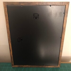 May include: A brown wooden picture frame with a black mat and a black hanging wire on the back.