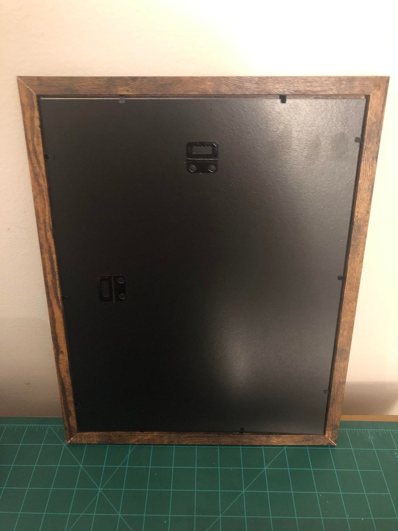 May include: A brown wooden picture frame with a black mat and a black hanging wire on the back.