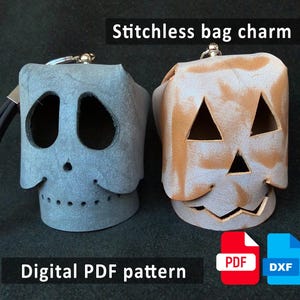 May include: Two leather bag charms, one gray skull-shaped and one tan pumpkin-shaped, with cut-out features. The charms have key rings and black straps. Text on the image reads "Stitchless bag charm" and "Digital PDF pattern".