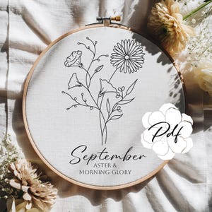 May include: A floral embroidery hoop featuring a black line drawing of aster and morning glory flowers. The text "September" and "ASTER & MORNING GLORY" is below the floral design. The hoop is set against a white fabric background.