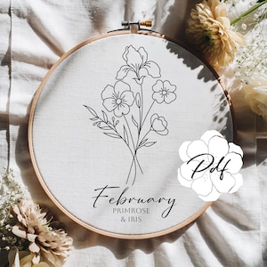 May include: An embroidery hoop with a floral design. The design features a black line drawing of primrose and iris flowers, with the text "February Primrose & Iris" below. The design is set against a white fabric background.