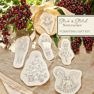 May include: A Nutcracker Crafting Gift Kit with six fabric patches featuring black line drawings of a ballerina, a Christmas tree, a rocking horse, and other characters. The kit includes an embroidery hoop and is surrounded by red berries.