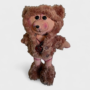 May include: A handmade plush teddy bear with a pink face, black button eyes, and a brown fur coat. The bear has a red heart-shaped pendant and matching fur boots. The bear is standing on a white background.