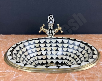 May include: A black and white oval sink with a geometric pattern. The sink has a brass rim and a brass faucet with a black and white geometric pattern.