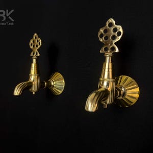 Puede incluir: Dos grifos de pared de latón dorado con detalles decorativos ornamentados. Los grifos tienen un caño con un diseño acanalado y un remate decorativo.