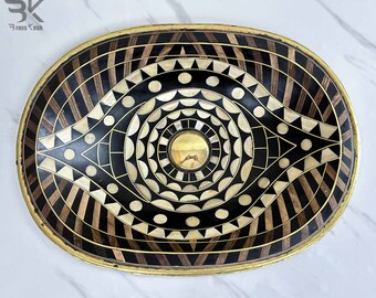 Op de afbeelding: Een ovale decoratieve dienblad met een zwart-wit geometrisch ontwerp. Het dienblad is gemaakt van hout en heeft een messing rand. Het midden van het dienblad heeft een cirkelvormig ontwerp met een messing midden.