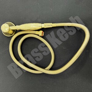 Pu&ograve; includere: Un set doccia color oro composto da soffione e flessibile. Il soffione &egrave; rotondo con una base piatta e un manico decorato. Il flessibile &egrave; arrotolato e collegato al soffione. Il set &egrave; su una superficie nera.