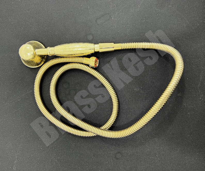 Pu&ograve; includere: Un set doccia color oro composto da soffione e flessibile. Il soffione &egrave; rotondo con una base piatta e un manico decorato. Il flessibile &egrave; arrotolato e collegato al soffione. Il set &egrave; su una superficie nera.