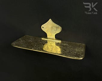 Puede incluir: Un estante de metal dorado con un diseño ornamentado. El estante está fijado a una pared con un soporte decorativo. El soporte tiene forma de arco apuntado con detalles intrincados.