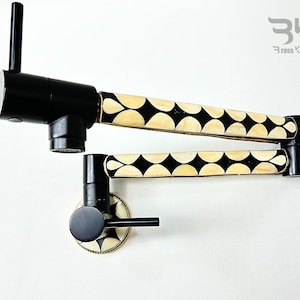 Puede incluir: Grifo de cocina negro con un diseño de patrón blanco y negro. El grifo tiene un pulverizador extraíble y una palanca. El grifo está montado en la pared.