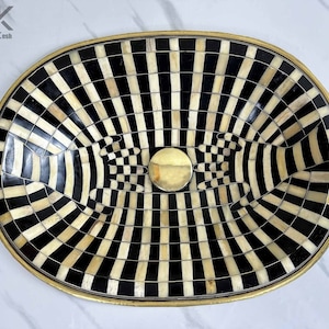 May include: An oval tray with a black and white striped design. The tray is made of bone and has a gold rim. The centre of the tray features a circular design with a gold centre.
