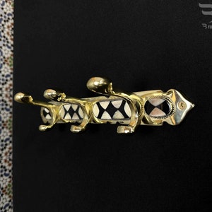 Peut inclure: Un porte-manteau en métal doré avec quatre crochets. Les crochets sont décorés de motifs géométriques noirs et blancs. Le porte-manteau est monté sur un mur noir.