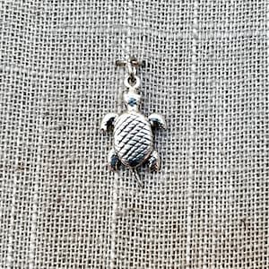 May include: A silver turtle charm with a detailed shell design. The charm is perfect for adding a touch of whimsy to jewelry or crafts.