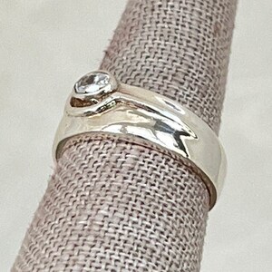 May include: A silver ring with a clear gemstone set in a curved band.