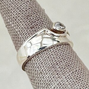 May include: A silver ring with a single clear stone set in a curved band.
