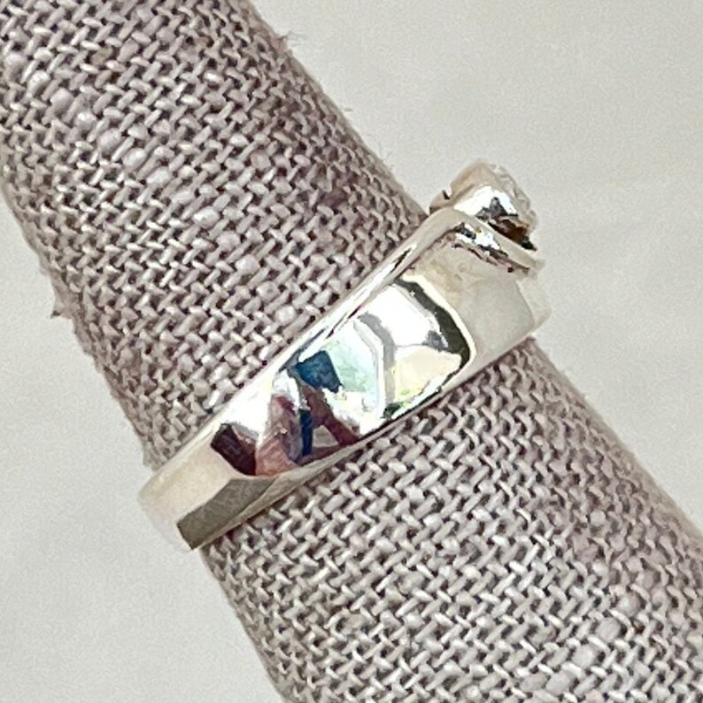 May include: A silver ring with a single round diamond set in a twisted band.