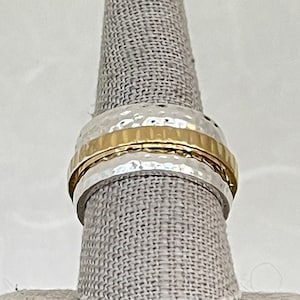 Peut inclure: Une bague en argent et or avec une texture martelée. La bague est sur un présentoir à bague en tissu.