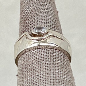May include: A silver ring with a clear gemstone set in a textured band.