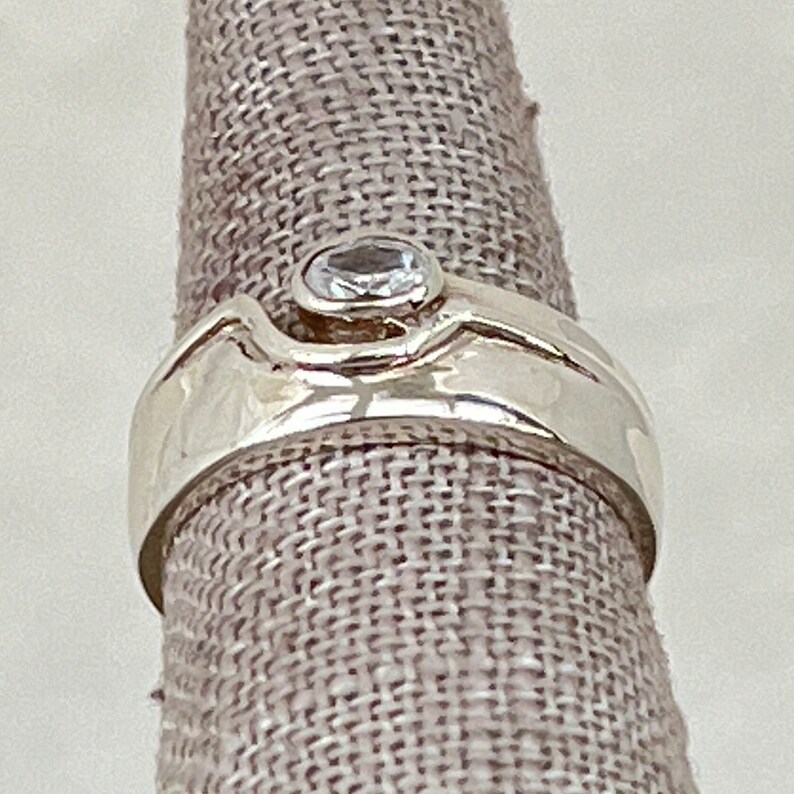 May include: A silver ring with a clear gemstone set in a textured band.