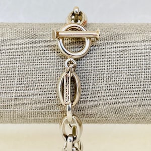 May include: A silver chain bracelet with a toggle clasp. The bracelet has a small oval tag with the text "Charles Albert" engraved on it.