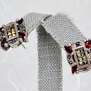May include: A pair of silver earrings with a rectangular marcasite stone surrounded by red garnet stones.