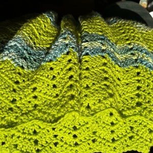 May include: A crocheted blanket with a green and blue striped pattern. The blanket is made with a delicate stitch and has a scalloped edge.
