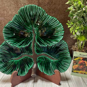 May include: A green ceramic serving dish shaped like a tree with three branches. The dish has a textured surface and is on a wooden stand. The dish is a vintage item and is perfect for serving snacks or appetizers.