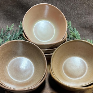 May include: Set of six brown and beige ceramic bowls. The bowls are all the same size and shape, and they have a slightly textured surface.