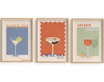 Puede incluir: Tres impresiones enmarcadas con ilustraciones de cócteles. La primera impresión es azul con estrellas blancas y el texto "Daiquiri". La segunda impresión es naranja con estrellas blancas y el texto "Espresso Martini". La tercera impresión es verde con estrellas blancas y el texto "Aperol Spritz".