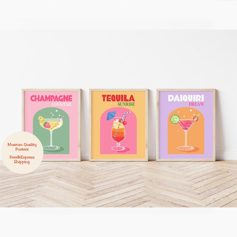 May include: Three colorful posters with illustrations of cocktails. The posters are framed in wood and have a pink, yellow, and purple background. The text on the posters reads "Champagne Cocktail", "Tequila Sunrise", and "Daiquiri Dream".