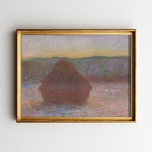 May include: A framed landscape painting featuring a large, reddish-brown haystack in a field. The artwork has a gold-colored frame and depicts a soft, pastel-colored sky and distant trees. The overall theme is rural and pastoral.