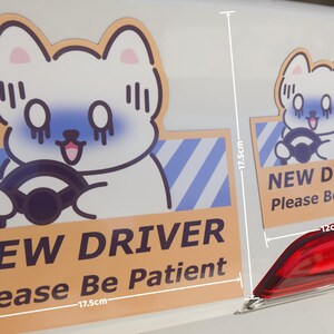 May include: Two rectangular car magnets featuring a cartoon white dog with blue shading driving a vehicle. The text reads NEW DRIVER Please Be Patient. The larger magnet measures 17.5cm by 17.5cm, and the smaller magnet measures 12cm by 12cm.