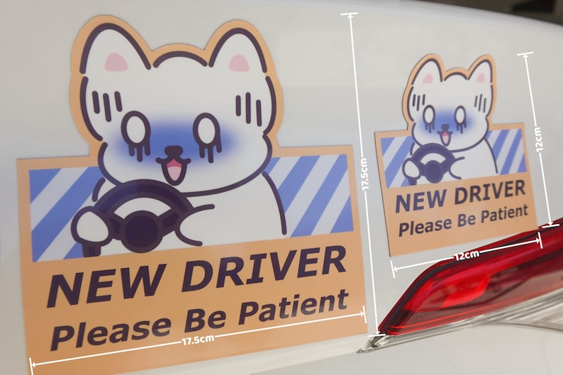 May include: Two rectangular car magnets featuring a cartoon white dog with blue shading driving a vehicle. The text reads NEW DRIVER Please Be Patient. The larger magnet measures 17.5cm by 17.5cm, and the smaller magnet measures 12cm by 12cm.