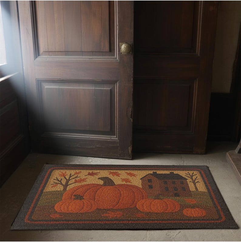 May include: Rectangular doormat featuring a fall harvest scene with pumpkins, a house, and trees. The mat has a dark brown border and a tan background. The pumpkins are orange, and the leaves are shades of orange and brown.