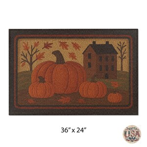 May include: Rectangular doormat featuring a fall harvest scene. The design includes three orange pumpkins, a brown house, and falling leaves. The mat measures 36 inches by 24 inches.
