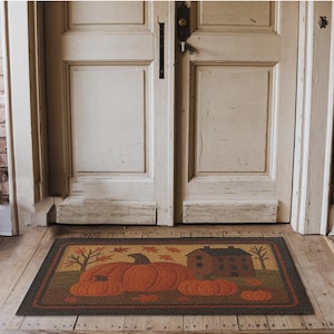 May include: Rectangular doormat featuring a fall harvest scene. The mat displays three large orange pumpkins, a small house, and trees with falling leaves. The border is dark brown, and the background is a mix of brown and tan.
