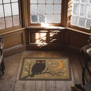 May include: A rectangular doormat featuring a dark brown owl perched on a branch with a crescent moon and stars. The mat has a tan background with a dark green border, perfect for a home's entryway.