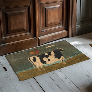 May include: A green, brown, and white doormat with a black and white cow and a red rooster on it. The doormat is in front of a wooden door.