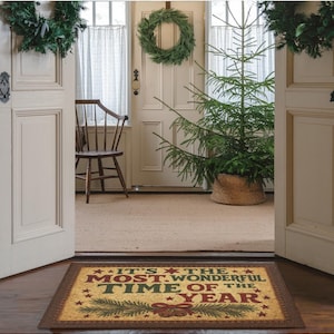 May include: A rectangular doormat with the text "IT'S THE MOST WONDERFUL TIME OF THE YEAR" in red and green. The mat has a brown border and a festive design with stars and a bow. The scene includes a Christmas tree, wreaths, and an open doorway.