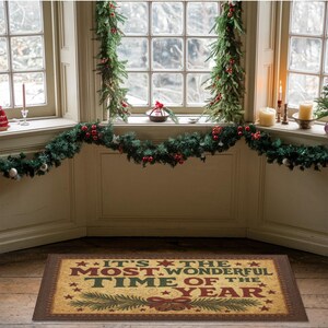 May include: A rectangular doormat with the text "IT'S THE MOST WONDERFUL TIME OF THE YEAR" in red, green, and gold. The mat features a festive design with stars, a pine branch, and a bow. The mat is placed in front of a window decorated with garland.
