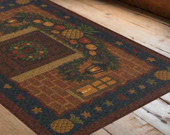 May include: Rectangular indoor rug with a detailed design. The rug features a central square with a wreath and a garland of fruits and pineapples. The border is dark blue with yellow stars and pineapples. The color palette includes brown, green, yellow, and red.